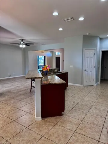 Kitchen featuring a center island with sink, ceiling fan, light tile patterned flooring, and a kitchen breakfast bar