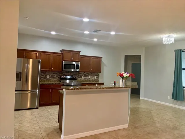 Kitchen with backsplash, an inviting chandelier, a center island with sink, dark stone countertops, and appliances with stainless steel finishes