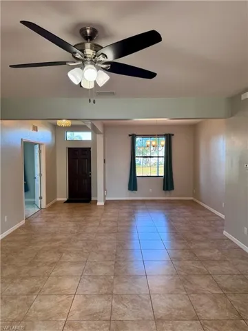 Tiled empty room featuring ceiling fan with notable chandelier