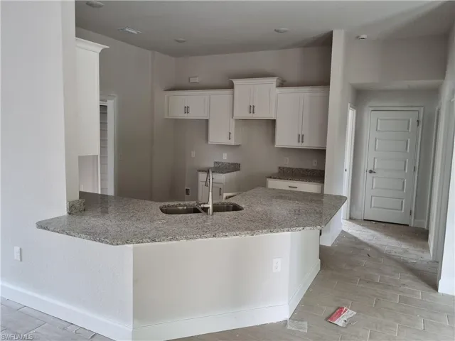 Kitchen with sink, light stone countertops, light wood-type flooring, white cabinetry, and kitchen peninsula