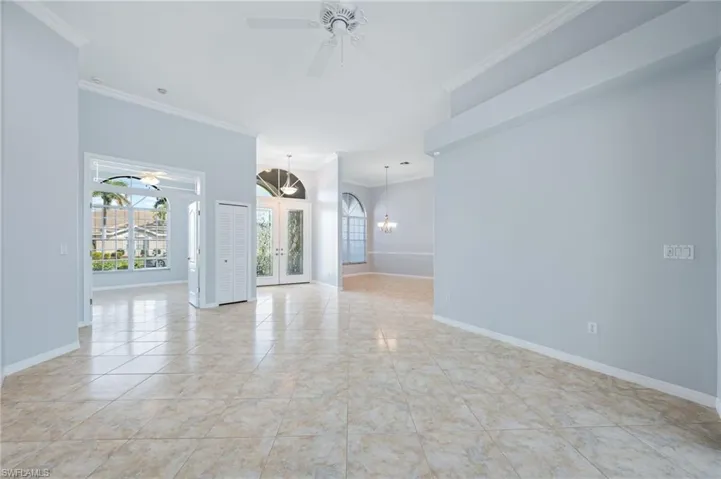 Unfurnished room featuring ceiling fan with notable chandelier, french doors, crown molding, light tile patterned floors, and baseboards