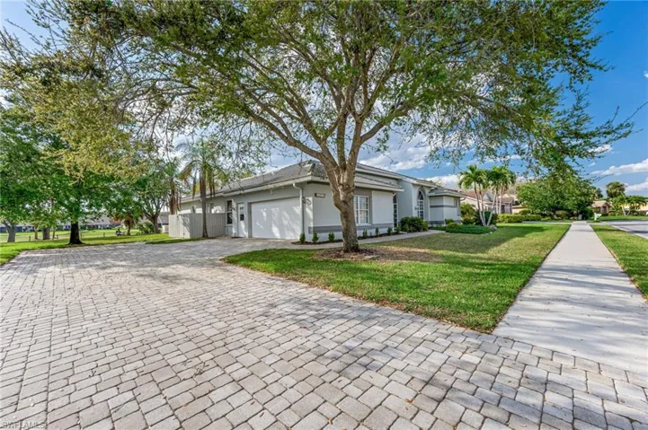 View of side of home featuring decorative driveway, an attached garage, a lawn, and stucco siding