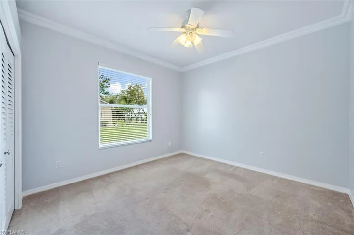 Spare room with ceiling fan, crown molding, baseboards, and light carpet