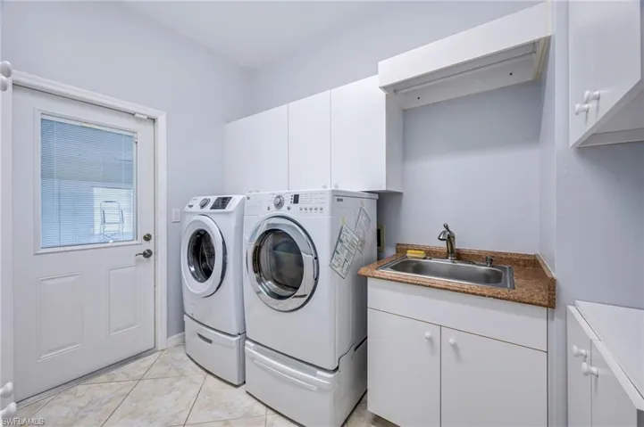 Laundry area featuring light tile patterned floors, cabinet space, independent washer and dryer, and a sink