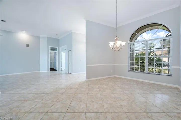 Spare room with tile patterned flooring, baseboards, crown molding, and an inviting chandelier