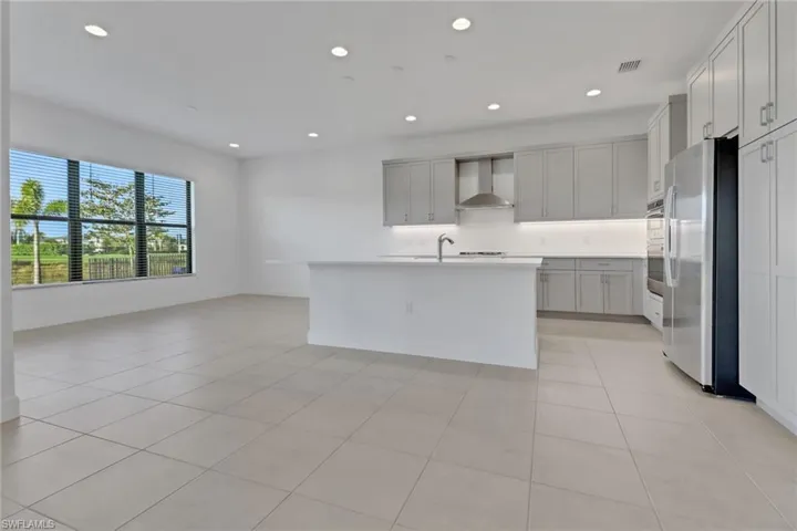Kitchen featuring freestanding refrigerator, wall chimney range hood, open floor plan, and recessed lighting
