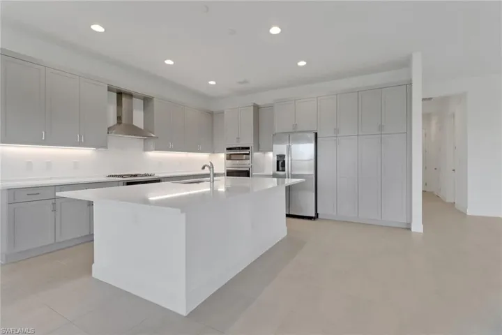 Kitchen with gray cabinetry, appliances with stainless steel finishes, a center island with sink, and wall chimney exhaust hood