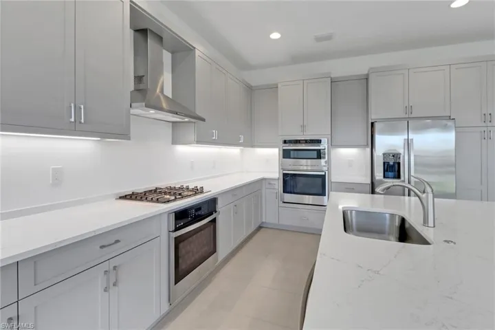 Kitchen featuring recessed lighting, light stone counters, a sink, wall chimney range hood, and stainless steel appliances
