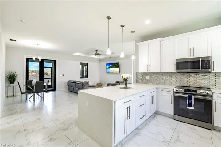 Kitchen with stainless steel appliances, open floor plan, light marble finish floors, white cabinetry, and tasteful backsplash