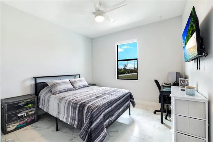 Bedroom with light marble finish flooring, a ceiling fan, and an office area