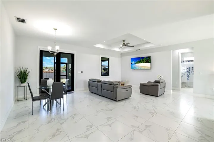 Living room with ceiling fan, a chandelier, a tray ceiling, and light marble finish flooring