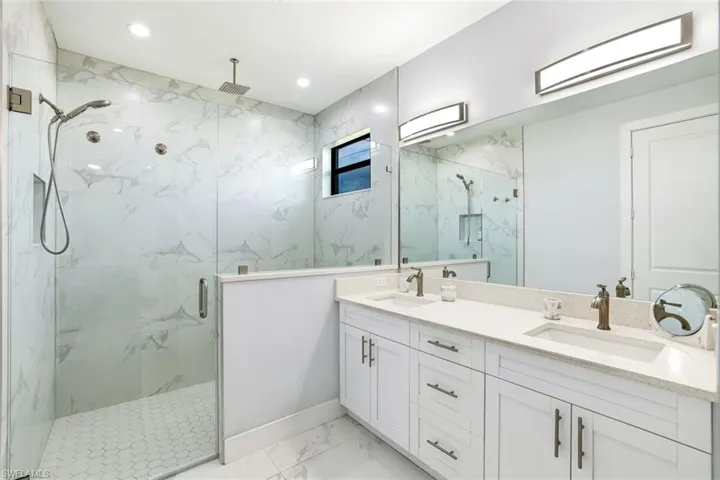 Bathroom featuring double vanity, a marble finish shower, and light marble finish floors