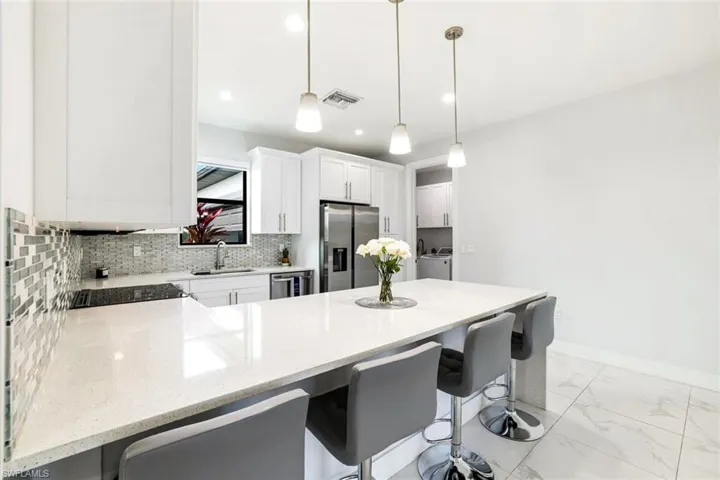 Kitchen with a peninsula, a kitchen bar, light stone countertops, stainless steel appliances, and white cabinetry