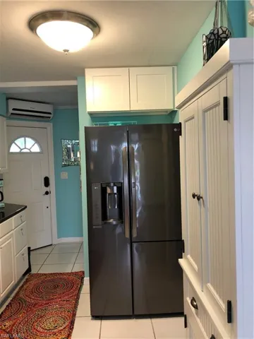 Kitchen featuring a wall mounted AC, white cabinets, light tile patterned floors, and black refrigerator with ice dispenser