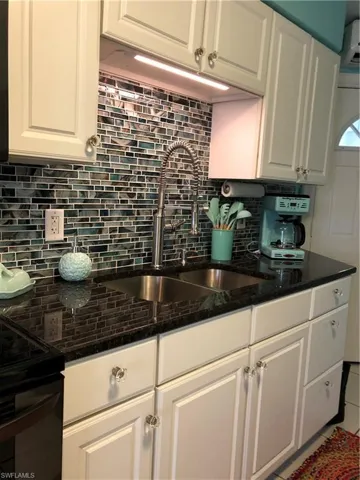 Kitchen with tasteful backsplash, white cabinets, and dark stone countertops