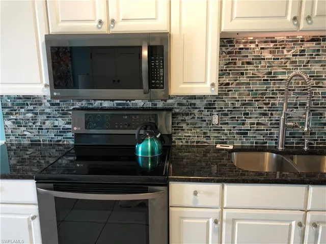 Kitchen with backsplash, dark stone countertops, appliances with stainless steel finishes, white cabinetry, and a sink