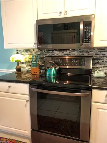 Kitchen featuring stainless steel electric range oven, backsplash, white cabinets, and dark stone counters