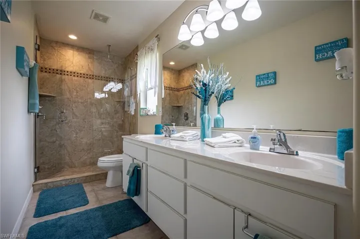 Bathroom with double vanity, a stall shower, toilet, tile patterned floors, and baseboards