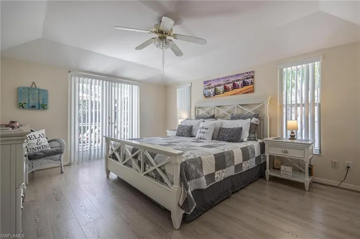 Bedroom featuring a raised ceiling, wood finished floors, a ceiling fan, access to exterior, and baseboards