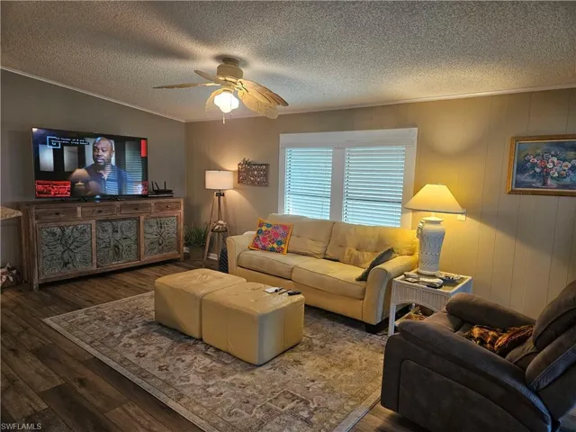 Living room with ceiling fan, a textured ceiling, wood finished floors, and ornamental molding