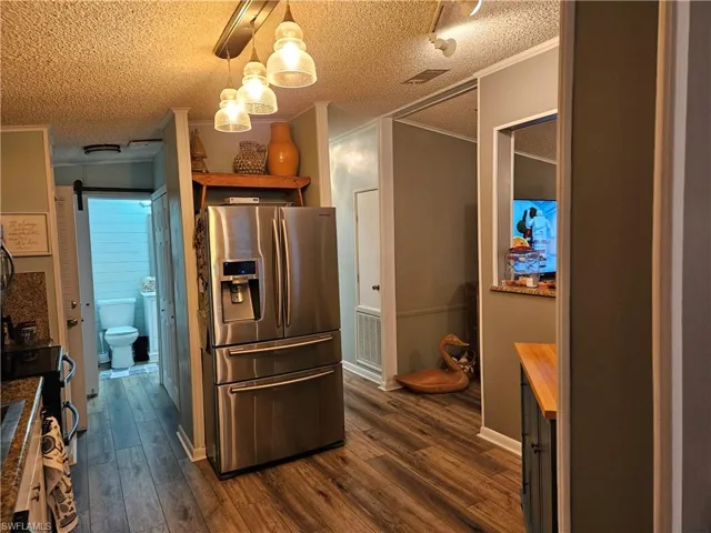 Kitchen featuring decorative light fixtures, stainless steel fridge, ornamental molding, and dark wood-type flooring