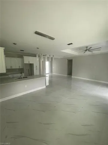 Unfurnished living room with sink, ceiling fan, and light tile floors