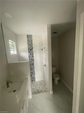 Bathroom featuring a tile shower, tile flooring, vanity, and toilet