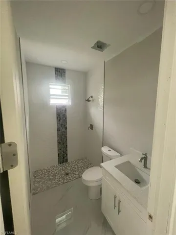 Bathroom with tile floors, vanity, a tile shower, and toilet