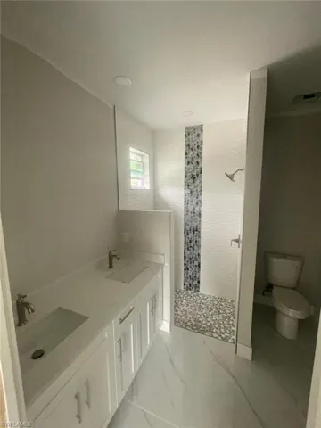 Bathroom featuring double sink vanity, tile flooring, tiled shower, and toilet