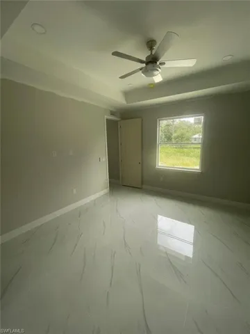 Empty room with a tray ceiling, ceiling fan, and light tile floors