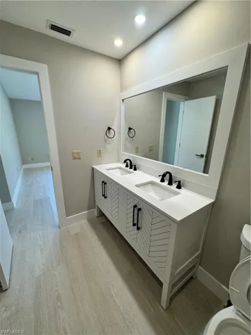 Bathroom with wood-type flooring, dual vanity, and toilet
