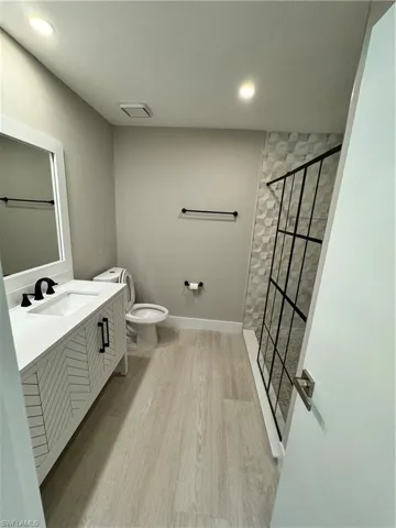 Bathroom with an enclosed shower, hardwood / wood-style flooring, vanity, and toilet