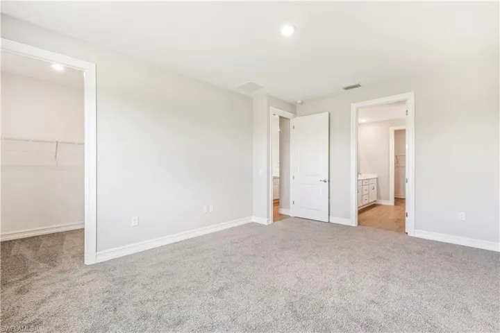 Unfurnished bedroom featuring a walk in closet, light carpet, ensuite bathroom, and recessed lighting