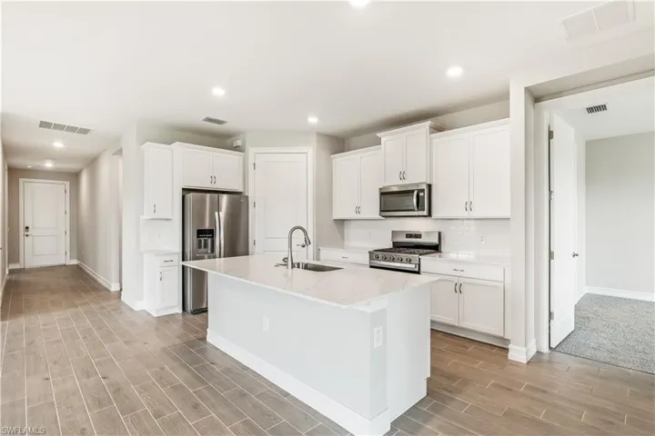 Kitchen with appliances with stainless steel finishes, recessed lighting, a center island with sink, white cabinetry, and backsplash