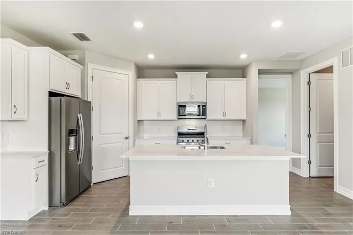Kitchen featuring wood tiled floors, appliances with stainless steel finishes, recessed lighting, white cabinets, and a center island with sink