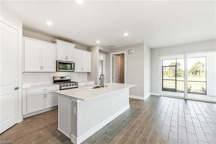 Kitchen featuring a kitchen island with sink, wood finish floors, stainless steel appliances, recessed lighting, and white cabinets