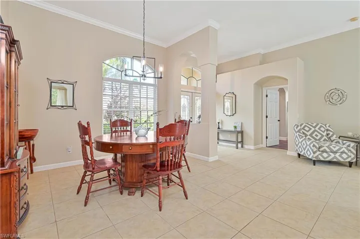 Dining room with french doors, arched walkways, light tile patterned flooring, ornamental molding, and hanging lights