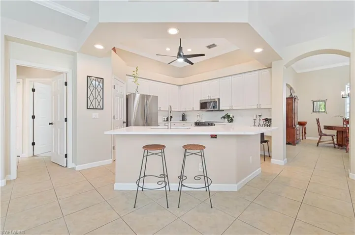 Kitchen with crown molding, a kitchen bar, light countertops, stainless steel appliances, and ceiling fan