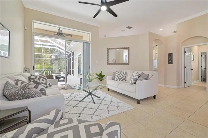 Living area with a sunroom, ornamental molding, ceiling fan, light tile patterned floors, and arched walkways