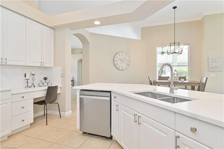 Kitchen with white cabinets, dishwasher, hanging light fixtures, light stone countertops, and arched walkways