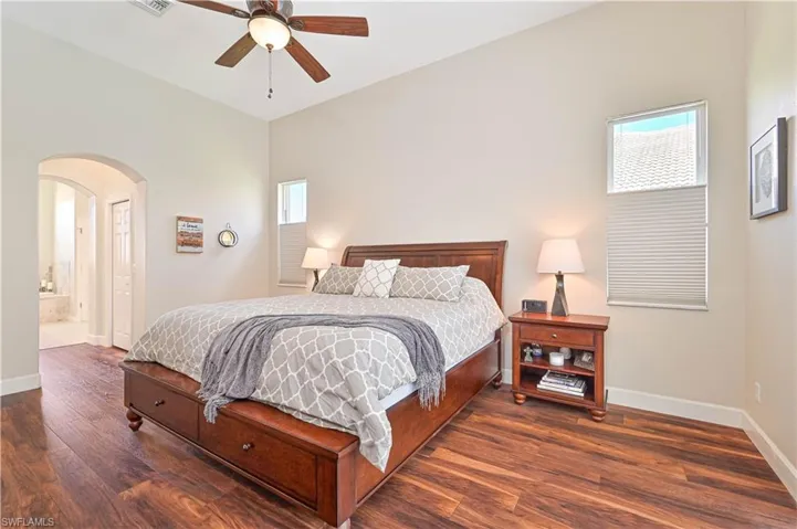Bedroom featuring arched walkways, connected bathroom, dark wood-style floors, and a ceiling fan