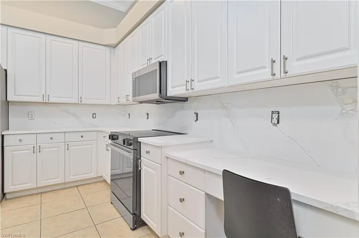 Kitchen featuring electric range oven, white cabinets, decorative backsplash, and light tile patterned floors