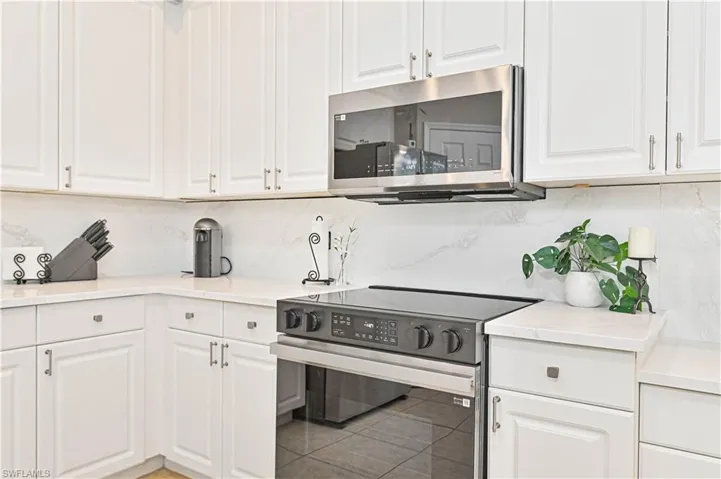 Kitchen featuring stainless steel appliances, white cabinetry, and light stone countertops