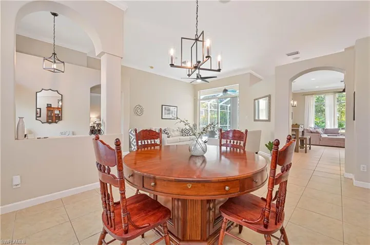 Dining space featuring arched walkways, light tile patterned flooring, suspended lighting, crown molding, and ceiling fan