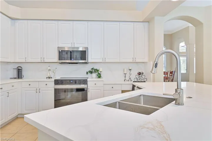 Kitchen with white cabinets, electric range, stainless steel microwave, light stone countertops, and ornamental molding