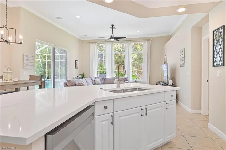 Kitchen with white cabinetry, open floor plan, light stone countertops, crown molding, and dishwasher