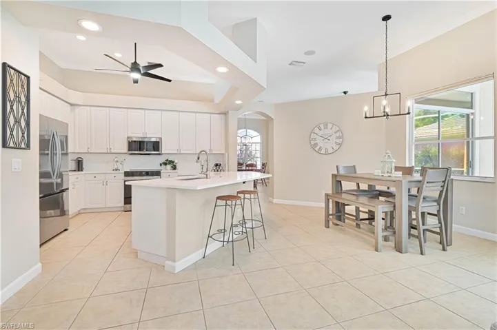 Kitchen with arched walkways, crown molding, stainless steel appliances, a kitchen bar, and ceiling fan