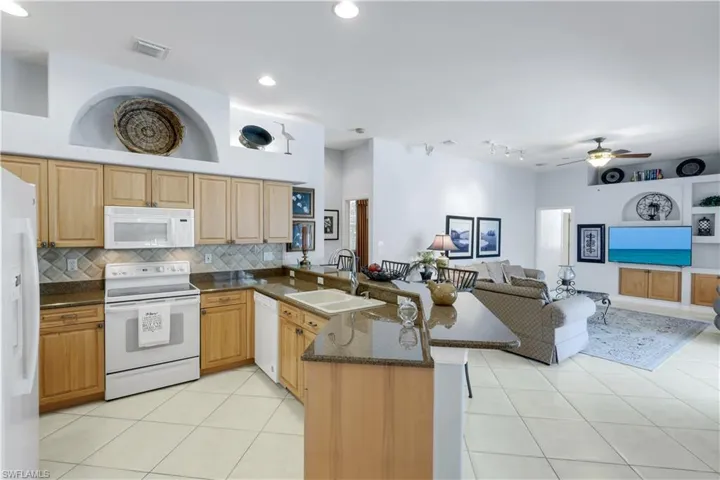 Kitchen featuring dark stone counters, white appliances, open floor plan, a peninsula, and light tile patterned floors