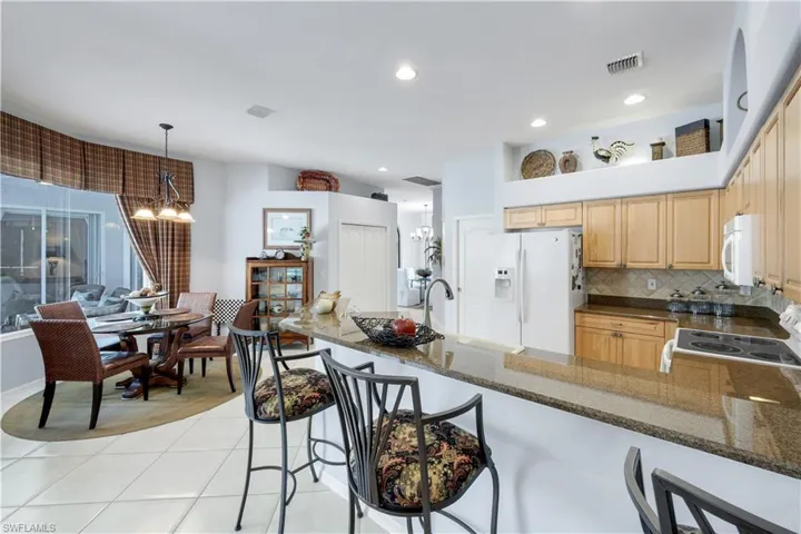 Kitchen with white appliances, a peninsula, a breakfast bar area, decorative backsplash, and decorative light fixtures
