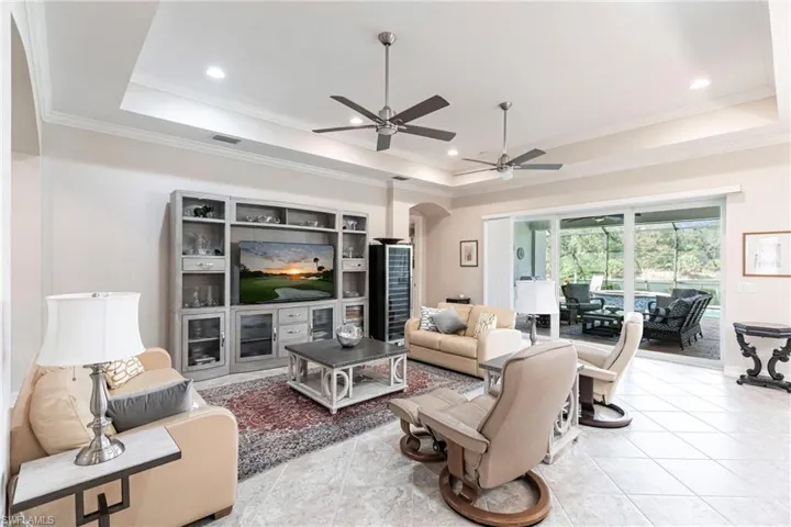 Tiled living room featuring a raised ceiling, ceiling fan, and crown molding